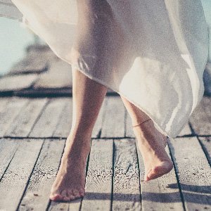 Close up of lady's legs in a floaty white dress wearing an anklet.