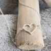Silver anklet with a charm of an outline of a heart displayed on wood.