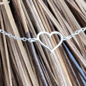 Silver heart charm on a silver anklet laying across straw.