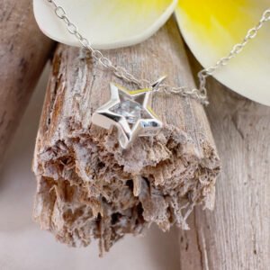 Stunning silver anklet with silver star charm with a big cubic zirconia stone in the centre, displayed on wood with a big white and yellow frangipani petal at the top of the photo.