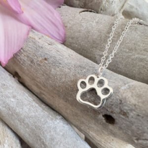 Cute puppy pawprint charm on a sterling silver anklet draped on some wood with a purple petal in the top left corner.