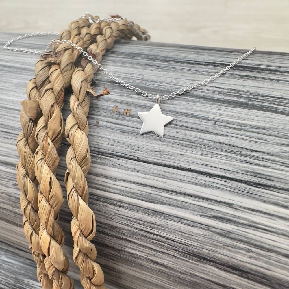 A17-Shine-Bright-Anklet-Sterling-Silver-(1) Sterling silver anklet with a silver star pendant draped over black and white wood with a twisted rope.