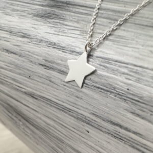 Solid silver dainty five pointed star charm on an anklet on a grey and white background.