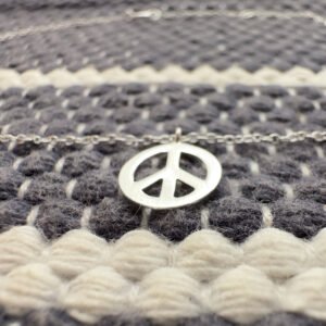 Silver anklet with a peace symbol charm on a blue and white wool background.