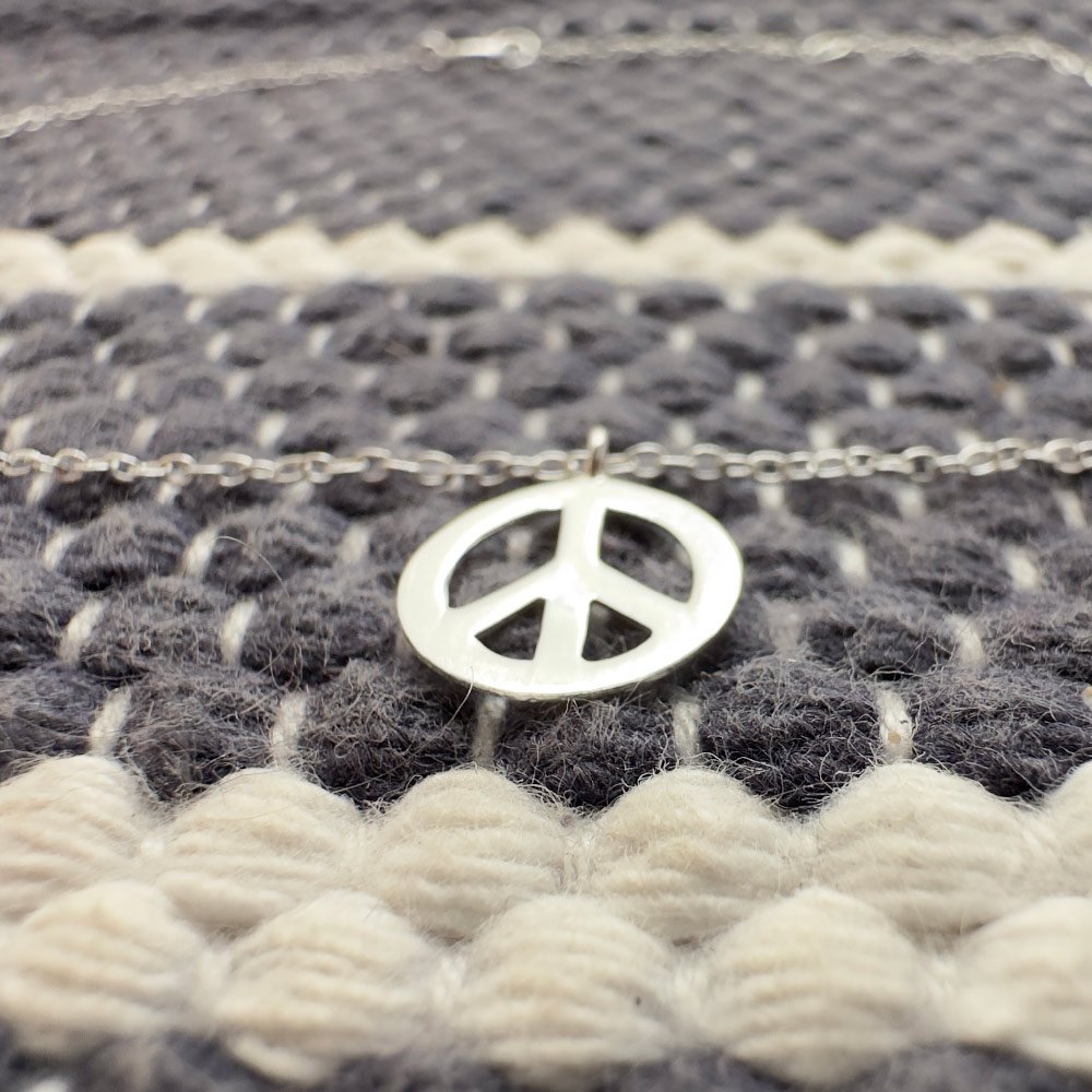 A19-Manifest-Peace-Anklet-Sterling-Silver-(1) Silver anklet with a peace symbol charm on a blue and white wool background.