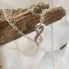 Silver anklet with infinity charm draped over some driftwood.
