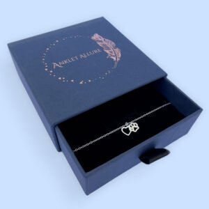 Silver anklet of a linked heart and pawprint, presented in a blue jewellery box with Anklet Allure written on the top in rose gold.