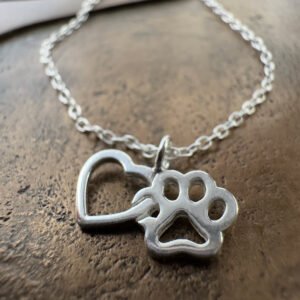 Close up of a sterling silver anklet with a heart linked to a pawprint charm.