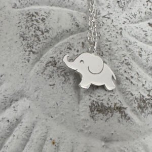 Close up of a cute shiny silver elephant charm on a sterling silver ankle chain on a white washed background.