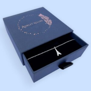 Elegant Parisien chic anklet in silver with a pendant of the Eiffel Tower, presented in a blue jewellery box with Anklet Allure written on the top in rose gold.