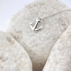 Close up of a silver anchor charm on a white rock.