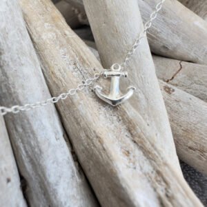 A silver anklet with a silver anchor charm displayed on white-washed sticks.
