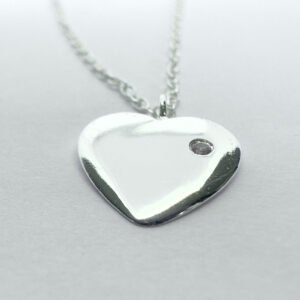 Close up of a heart charm with a dainty gemstone on a silver ankle bracelet.