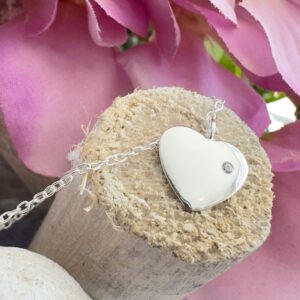 Solid sterling silver anklet with a heart charm with a dainty white gem displayed on the end of a stick with purple petals in the top right background.