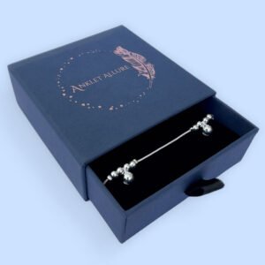 Silver anklet with large round charms with two smaller round charms either side, presented in a blue jewellery box.