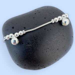 Silver anklet with large round charms with two smaller round charms either side, presented on a black rock.