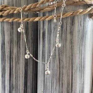 Silver anklet with jingling balls on a silver chain designed to look twisted, on a black and white painted wood background with rope around the top.