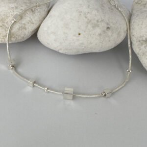 Ankle bracelet in silver with different sized square charms on white rocks.