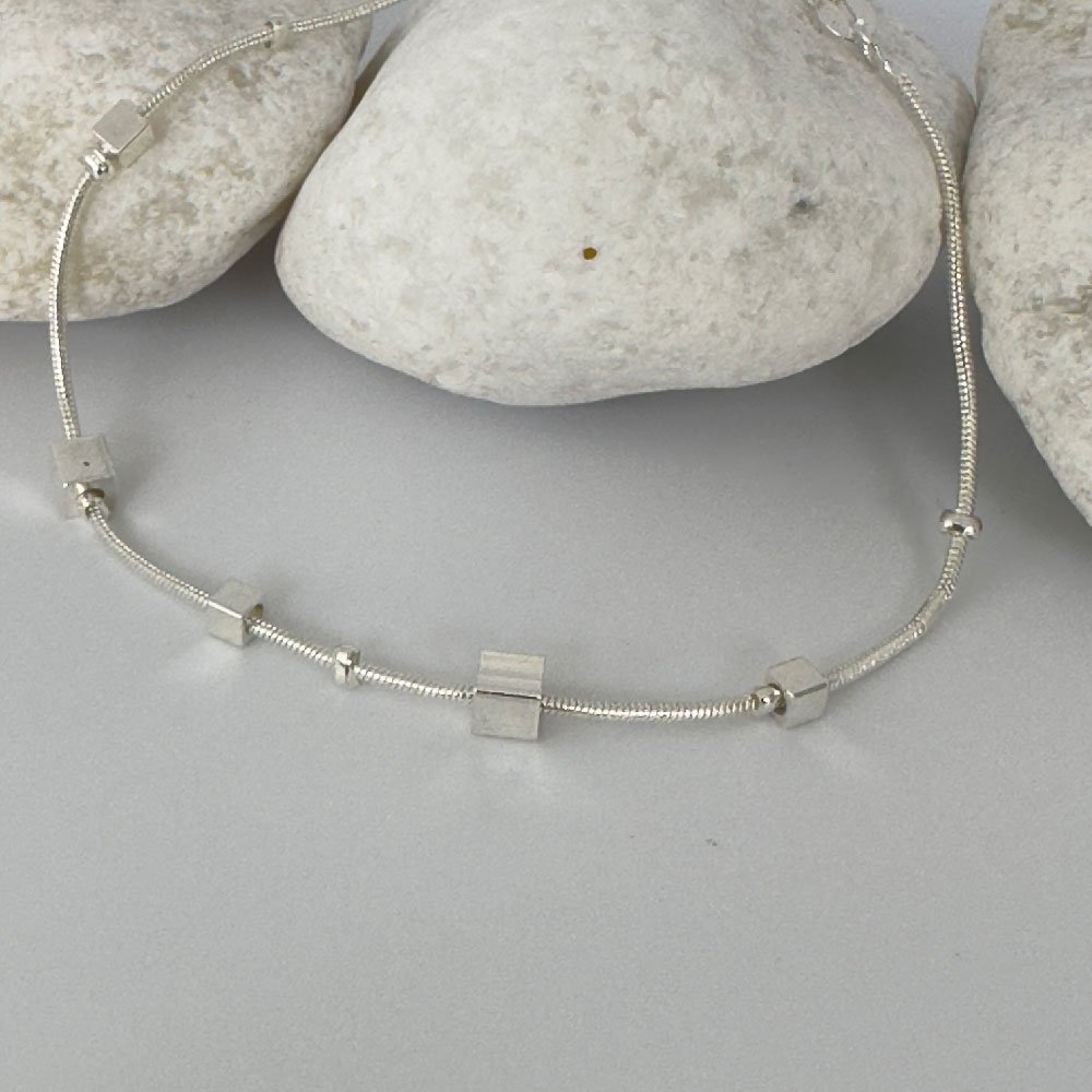 B2-Anklet-(3) Ankle bracelet in silver with different sized square charms on white rocks.