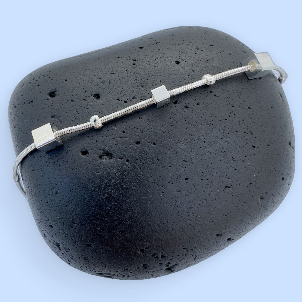 B2-Anklet-rock Ankle bracelet in silver with different sized square charms on a black rock.