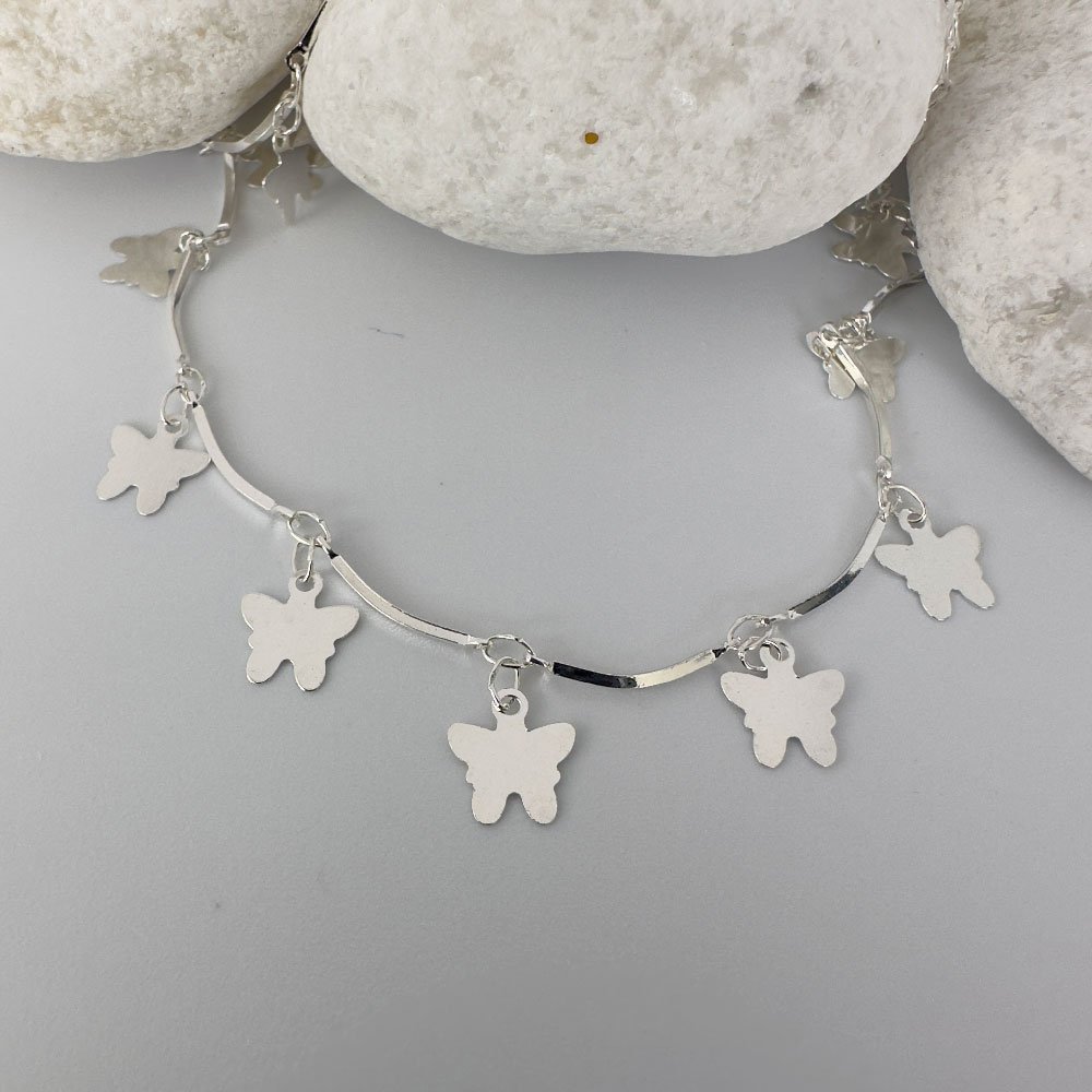 B3-Anklet-(1) Stiff silver ankle chain with solid butterfly charms on white rocks.