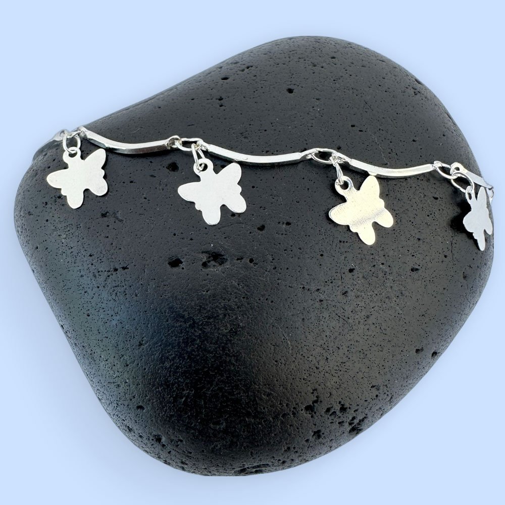 B3-Anklet-rock Stiff silver ankle chain with solid butterfly charms on a black rock.