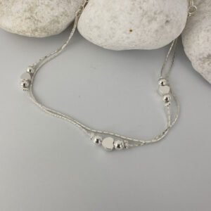Double chain silver anklet with a heart in between two silver balls on each chain on a white rock.