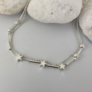 Stunning double chain silver ankle bracelet with three star charms and two small frosted ball charms either side on white rocks.