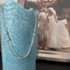 Silver anklet with a mix of small silver balls and silver stars, hanging over a blue candle with a couple kissing on their wedding day in the background.