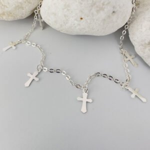 Silver anklet with three silver crosses equally spaced around the chain on a white rock.
