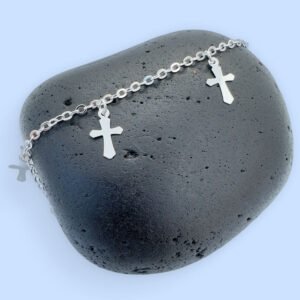 Silver anklet with three silver crosses equally spaced around the chain on a black rock.