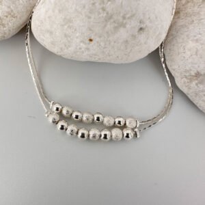 Silver anklet with a double chain with eight balls on a white rock.