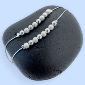 Double silver anklet chain both with eight silver balls on a black rock.