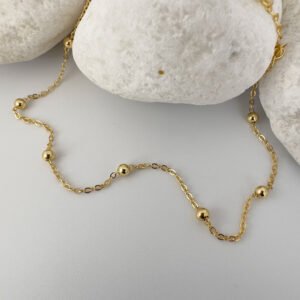 Gold chain with eight small gold balls on a white rock.