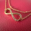 Close up of a gold infinity charm covered with cubic zirconia gems along one half, on a stunning gold ankle bracelet.
