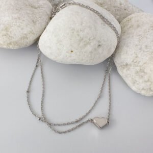 Double silver ankle bracelet with a solid silver heart displayed on white rocks.