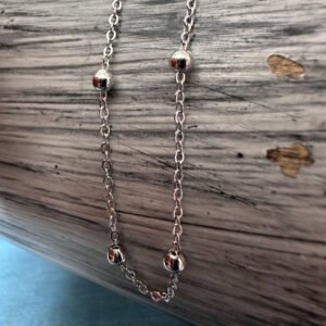 Silver anklet with four silver balls evenly spaced around the anklet draped om a white and grey painted wood background.