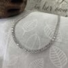 White diamond tennis anklet on grey and white leaf background.