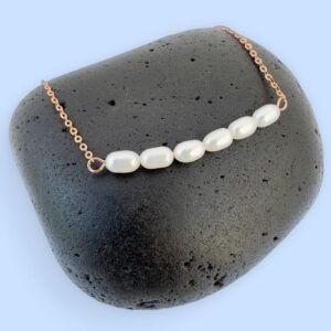 Rose gold anklet with six freshwater pearls sat on a black rock.