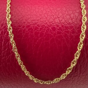 Close up of a simple gold anklet chain on a red background.