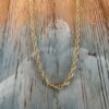 Looking up at a simple gold ankle bracelet hanging on a painted wood background with a beach chic feel.
