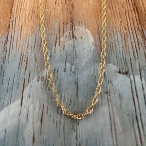 Looking up at a simple gold ankle bracelet hanging on a painted wood background with a beach chic feel.