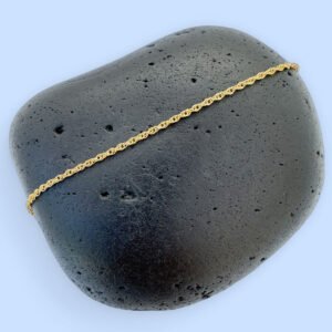 Dainty gold simple ankle bracelet presented on a black rock.