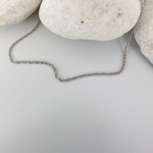 Plain silver anklet draped on three white rocks.