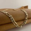 Stunning diamond cut figaro chain gold anklet pictured close up draped over a mustard coloured purse.