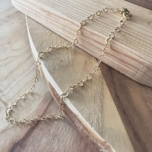 Loving gold hearts interlinked to form a beautiful anklet, presented on wood.