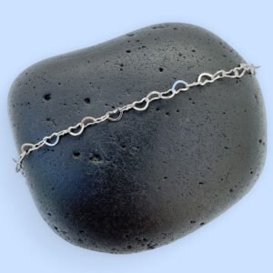 Identical silver hearts interlinked to make a dainty anklet displayed on a rock.