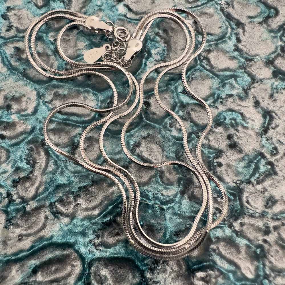 D1-Faith-Hope-&-Charity-Anklet Triple chain sterling silver anklet curled up on a blue and silver background like spaghetti.