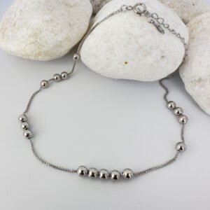 Silver anklet with identical balls floating around the chain, on white rocks.
