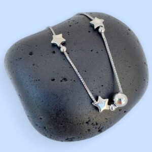 Silver anklet with solid star and ball charms on a black rock.